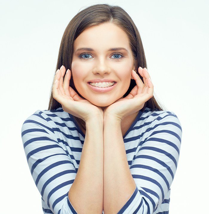 Woman with clear and ceramic braces framing her smile with her hands