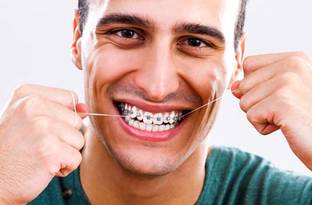 Man with braces flossing to prevent orthodontic emergencies in Lawrence