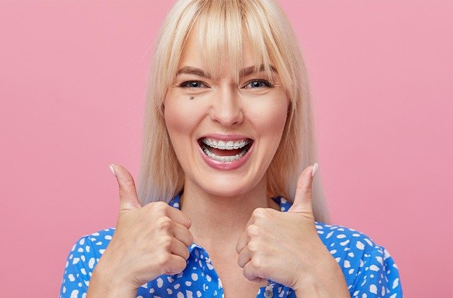 Woman with braces smiling and giving two thumbs up