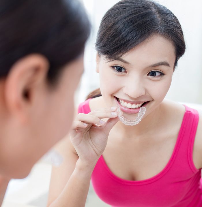 Woman looking in the mirror as she places an Invisalign tray
