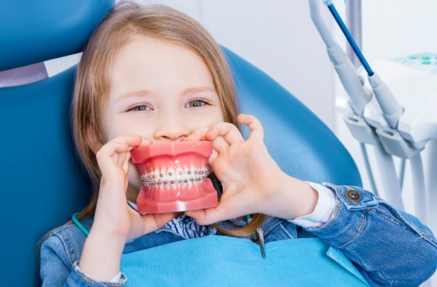 Child in dental chair, holding model with braces