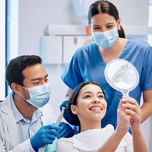 Woman smiling at reflection in handheld mirror with dental team