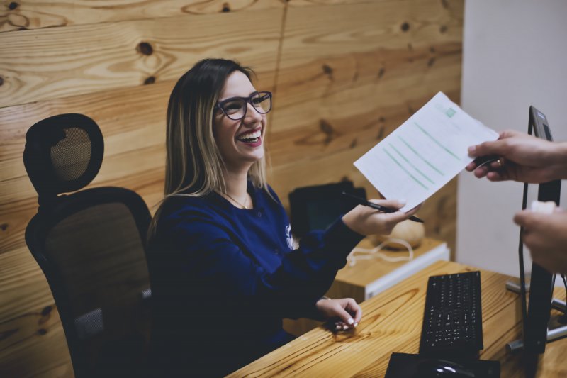 Dental receptionist smiling while handing patient paperwork