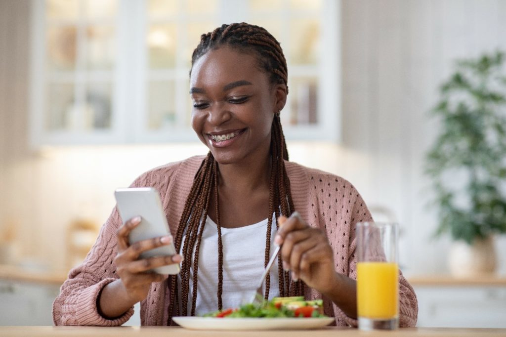 Woman with braces eating lunch while checking her phone