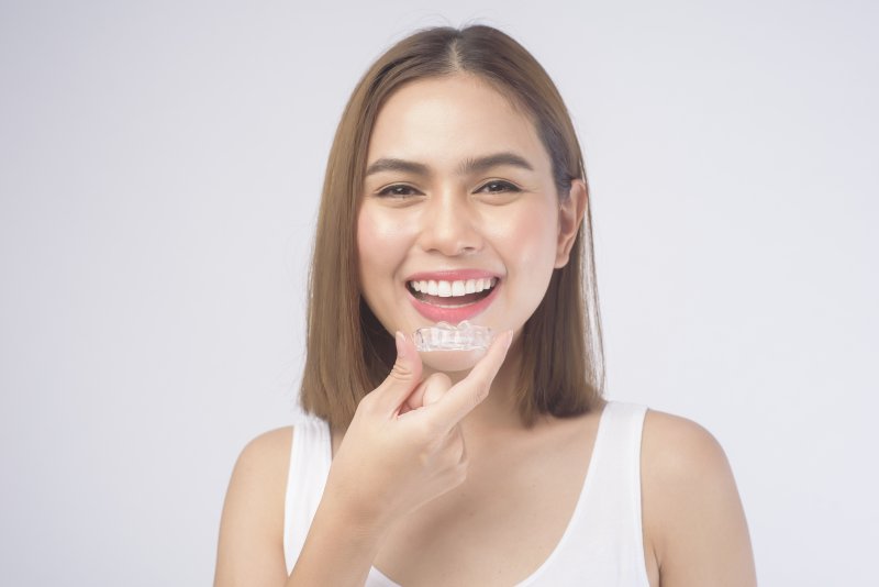 Woman smiling while putting in Invisalign clear aligners