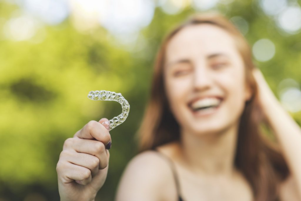 Woman smiling while holding Invisalign in Lawrence