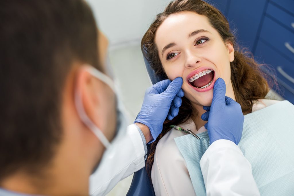 Woman with braces smiling while orthodontist examines her smile