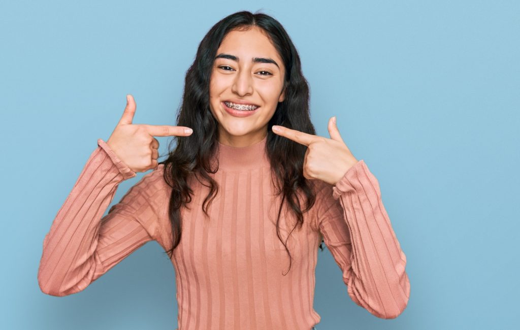 Girl in salmon shirt pointing to her braces and smiling